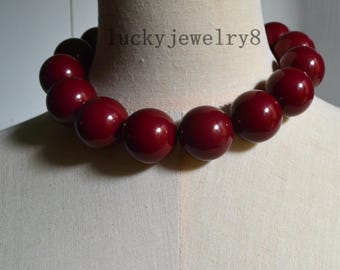 Può includere: Una collana chunky con grandi perle rotonde e lucide di colore bordeaux intenso. Le perle sono infilate insieme per formare un gioiello importante. Il testo "lucky jewelry8" è visibile sul manichino.