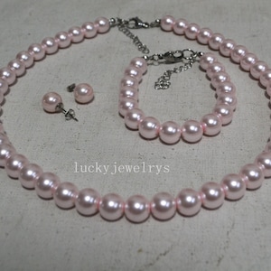 May include: A light pink pearl jewellery set comprising a necklace, bracelet, and stud earrings. The necklace and bracelet have silver-toned clasps. The earrings have silver posts. The text "lucky jewelrys" is visible.