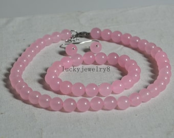 Puede incluir: Un conjunto de collar, pulsera y pendientes de piedras preciosas rosas. El collar y la pulsera están hechos de cuentas redondas, y los pendientes son simples tachuelas.