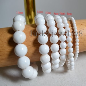 Könnte beinhalten: Mehrere weiße Perlenarmbänder in verschiedenen Größen werden gezeigt. Die Perlen haben einen Durchmesser von 4 mm bis 14 mm. Der Text "lucky jewelry8" ist sichtbar. Die Armbänder sind aufgereiht und zeigen eine Reihe von Größen.