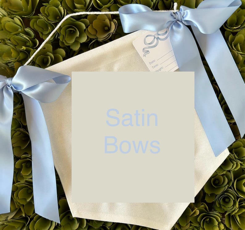 May include: A white canvas banner with the text "Satin Bows" printed in light blue. The banner is decorated with two light blue satin bows.