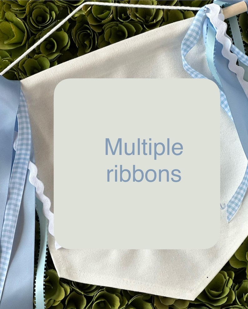 May include: A white canvas banner with the text "Multiple ribbons" printed in blue. The banner has blue and white gingham ribbon, blue satin ribbon, and white scalloped ribbon attached to it.