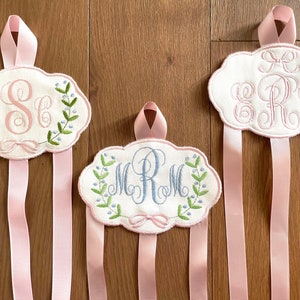 K&ouml;nnte beinhalten: Drei wei&szlig;e Stoff-Haarb&auml;nderhalter mit rosa Schleifen. Jeder Halter hat ein anderes besticktes Monogramm mit floralen Akzenten. Die Monogramme sind "ESG", "MCM" und "ERR".
