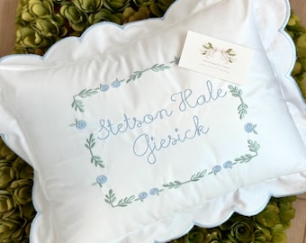 May include: White pillow with a blue scalloped edge and embroidered with a floral wreath and the name "Stetson Hale Giersick".