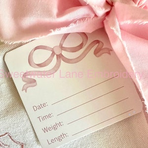 Peut inclure: Une carte blanche avec un motif de n&oelig;ud rose en aquarelle. La carte porte les mots "Date:", "Heure:", "Poids:" et "Longueur:" imprim&eacute;s dessus.