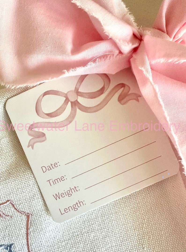 Peut inclure: Une carte blanche avec un motif de n&oelig;ud rose en aquarelle. La carte porte les mots "Date:", "Heure:", "Poids:" et "Longueur:" imprim&eacute;s dessus.