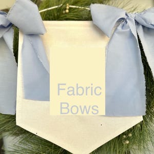 May include: A white fabric banner with the text "Fabric Bows" in light blue lettering. The banner is decorated with two large, light blue fabric bows.