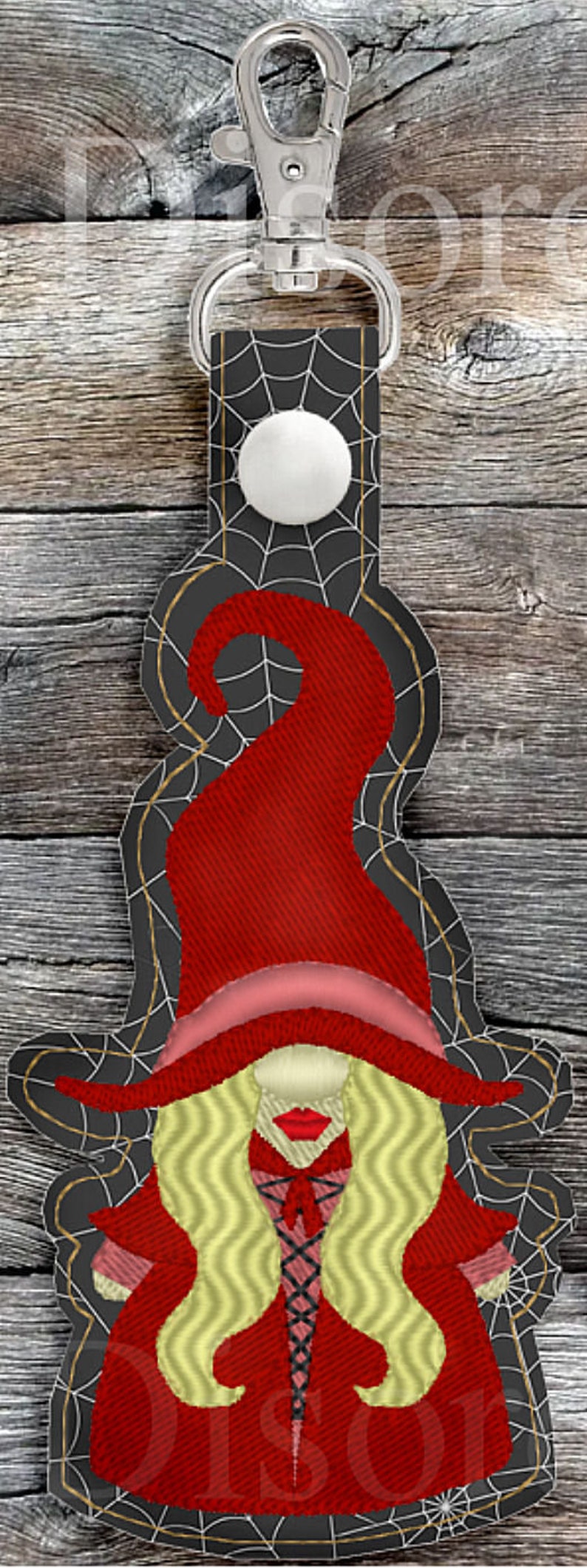 May include: A red and black witch gnome keychain with a spiderweb design. The gnome is wearing a red hat and a red dress with a black lace-up bodice. The gnome has long blonde hair.