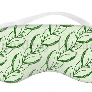 Può includere: Una maschera per dormire verde e bianca con un motivo a foglie. La maschera ha un cinturino elastico.