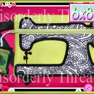 May include: A green and black sewing machine zipper pouch with a black and white patterned design. The pouch is 15.24 x 21.59 cm and has a green zipper and a black strap with a green spool of thread attached.
