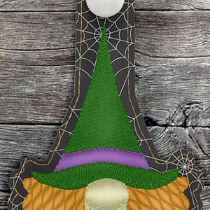 May include: A witch key chain with a green hat, purple dress, and orange hair. The witch is surrounded by a black spider web design.
