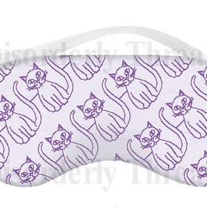 May include: White sleep mask featuring a repeating pattern of purple cat illustrations. The mask has a white elastic strap. The text "Disorderly Threads" is visible in the background.