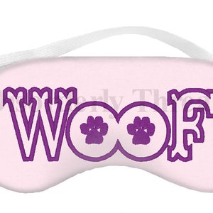 Op de afbeelding: Een roze slaapmasker met een paars geborduurd "WOOF" met poot afdrukken in de "O"s.