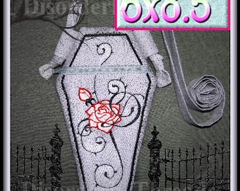 May include: A white coffin-shaped zippered pouch with a black embroidered rose and swirls. The pouch has a black strap and measures 6x8.5 inches.