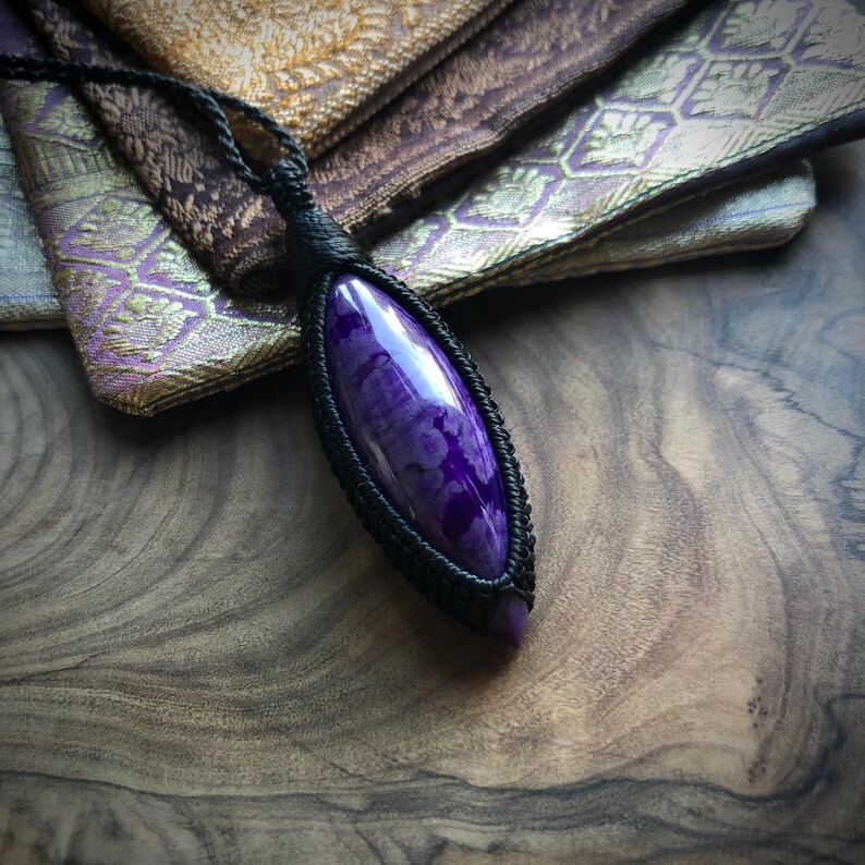 May include: A purple and white agate gemstone pendant wrapped in black cord. The pendant is shaped like a teardrop and has a glossy finish.