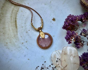 May include: A circular pendant necklace featuring a translucent pink stone encased in brown macrame cord. The pendant is attached to a brown cord necklace accented with small gold-toned beads and a decorative gold-toned metal bail at the top.