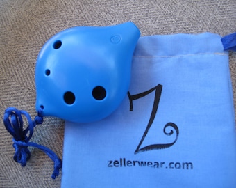 May include: A bright blue ocarina with four finger holes and a drawstring bag. The bag is light blue with the text "Z" and "zellerwear.com" printed in black.