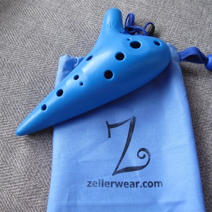 May include: A blue plastic ocarina with six finger holes and a carrying bag. The bag is blue with a white "Z" and the text "zellerwear.com".