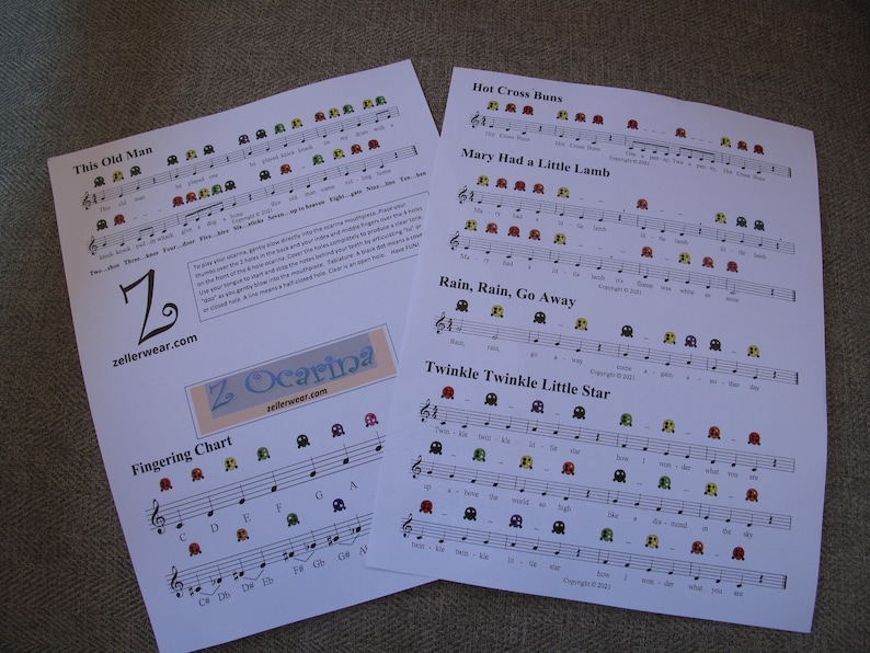 May include: Printable sheet music for the songs "This Old Man", "Hot Cross Buns", "Mary Had a Little Lamb", "Rain, Rain, Go Away", and "Twinkle Twinkle Little Star" with corresponding finger positions for a Z Ocarina. The sheet music is printed on white paper with black lines and colorful Pac-Man-like symbols.
