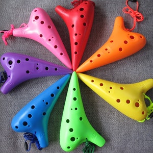 May include: A set of seven colorful ocarinas, each with a different color and a string attached. The ocarinas are arranged in a circle, with the tips of each ocarina pointing towards the center of the circle.