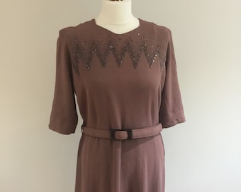 Könnte beinhalten: Ein mauvefarbenes Midikleid mit geometrischem Perlenbesatz am Ausschnitt und einem passenden Gürtel.