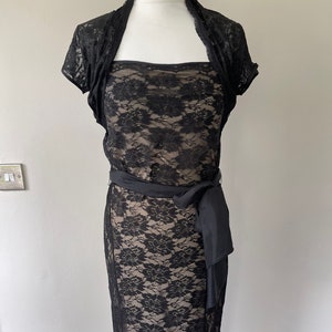 May include: A black lace dress with a matching lace shrug and a black satin sash. The dress has a strapless bodice and a fitted skirt.