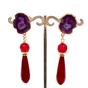 May include: A pair of dangle earrings with purple agate stone and red gemstone drops. The earrings are on a gold stand.