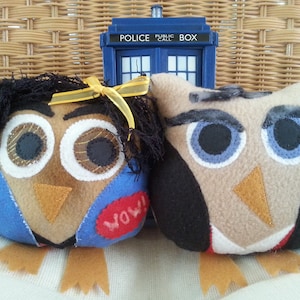 May include: Two plush owl toys, one blue and one brown, with large eyes and a 'WOW!' patch on the blue owl. The owls are sitting in front of a blue police call box.