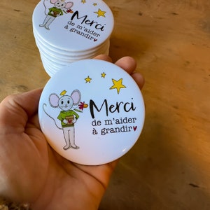 May include: White round button featuring a cartoon mouse holding a potted plant. The button reads "Merci de m'aider à grandir" with a small heart symbol.