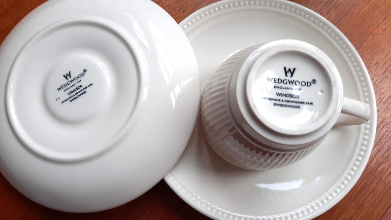 May include: White Wedgwood Windsor teacup, saucer, and plate set. The teacup has a ribbed design and a handle. The saucer and plate have a beaded edge. The bottom of the teacup and saucer have the Wedgwood logo and text.