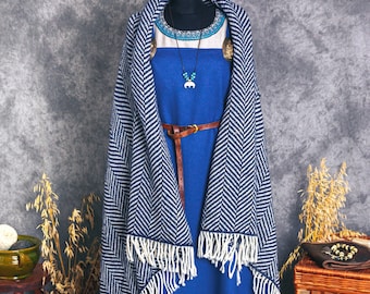 May include: A blue and white patterned dress with a brown leather belt and a blue and white patterned shawl. The dress has a white bottom with a blue and white embroidered trim. The dress is on a mannequin and is displayed on a gray background.