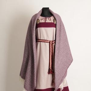 K&ouml;nnte beinhalten: Ein mittelalterliches Kleid und Schal-Set auf einer Schaufensterpuppe. Das Kleid ist haupts&auml;chlich hellrosa mit einem dunkelburgunderfarbenen Band am Saum und an der Brust. Ein passender Schal mit Rautenmuster ist &uuml;ber die Schultern drapiert. Ein dekorativer G&uuml;rtel und Broschen vervollst&auml;ndigen das Ensemble.