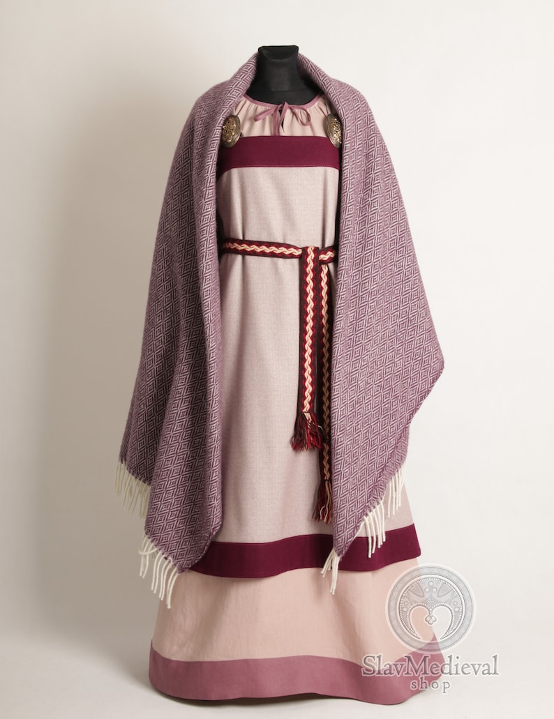K&ouml;nnte beinhalten: Ein mittelalterliches Kleid und Schal-Set auf einer Schaufensterpuppe. Das Kleid ist haupts&auml;chlich hellrosa mit einem dunkelburgunderfarbenen Band am Saum und an der Brust. Ein passender Schal mit Rautenmuster ist &uuml;ber die Schultern drapiert. Ein dekorativer G&uuml;rtel und Broschen vervollst&auml;ndigen das Ensemble.