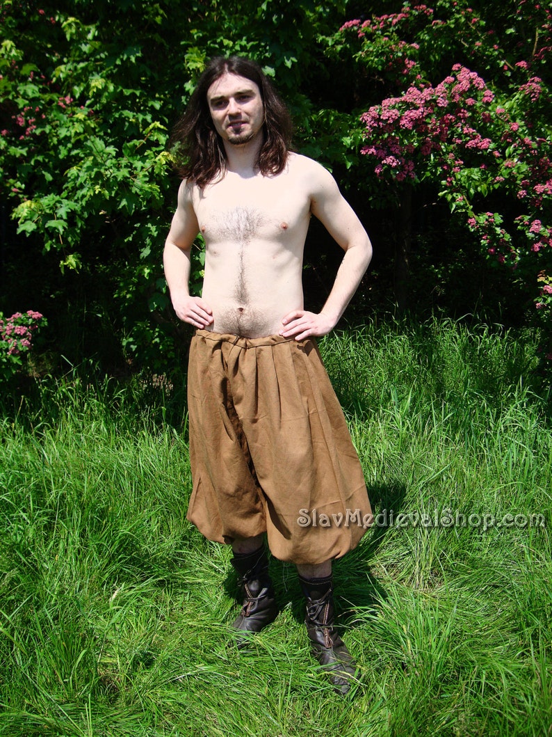 May include: A person wearing brown linen pants with a gathered waist and brown leather boots. The pants are loose fitting and have a wide leg. The person is standing in a field of green grass.