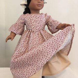 May include: A doll wearing a white bonnet and a red and white floral dress with a tan underskirt.
