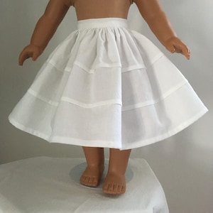 Puede incluir: Una falda de muñeca de algodón blanco con varias capas y una cintura fruncida.