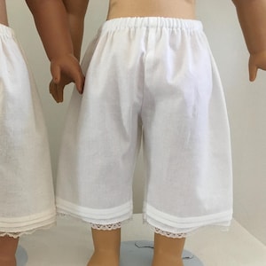 Puede incluir: Pantalones de muñeca de algodón blanco con ribete de encaje. Los pantalones tienen una cintura elástica y están hechos de una tela suave y ligera.