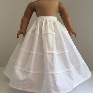 Puede incluir: Una falda de muñeca blanca con un diseño escalonado. La falda está hecha de una tela suave y tiene una forma completa y fluida. La muñeca lleva la falda, y la falda es el punto focal de la imagen.