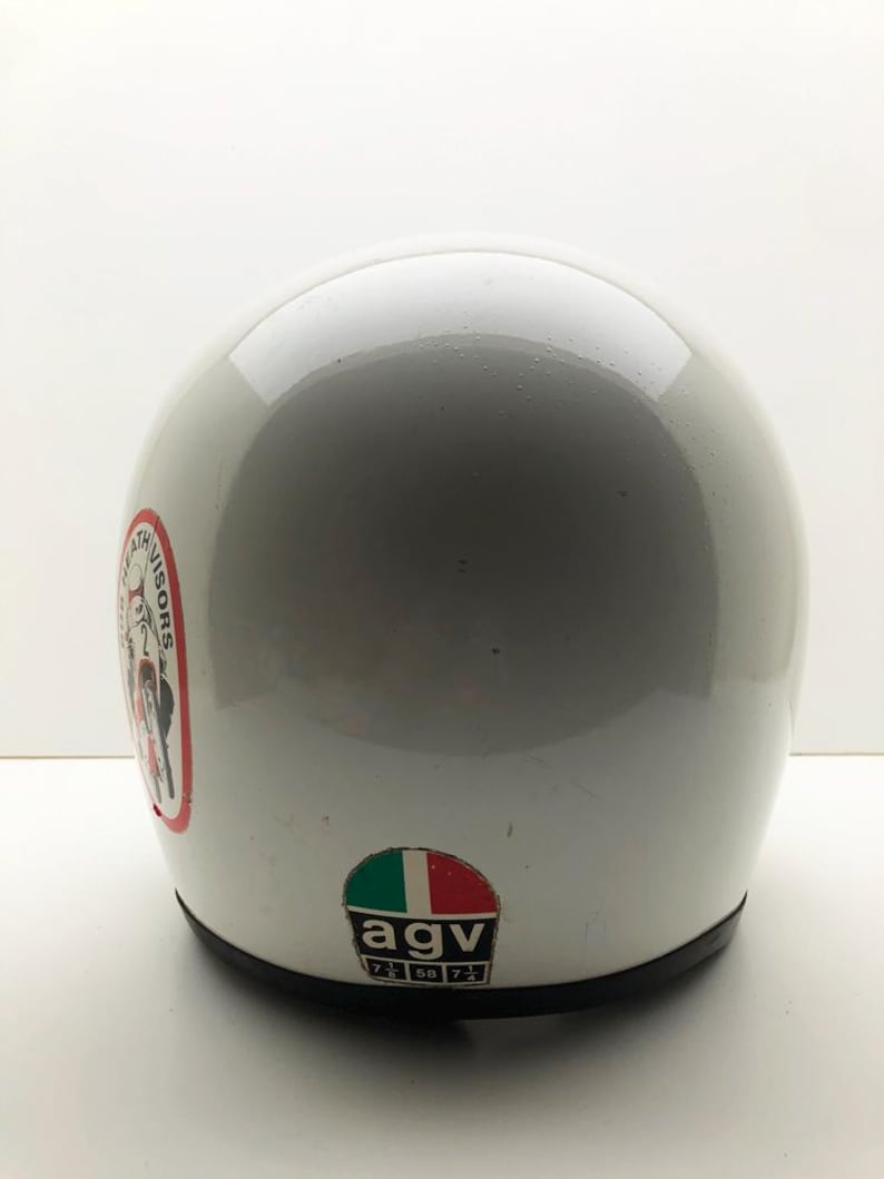 May include: A white motorcycle helmet with a glossy finish. The helmet has a black trim and features two stickers: one with a red, white, and black design and text, and another with the Italian flag and the letters "agv".