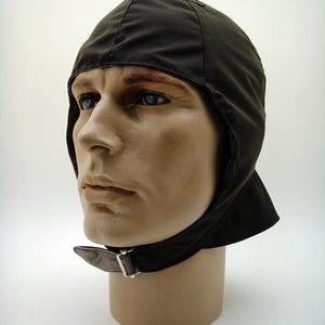 Puede incluir: Un gorro de aviador de color marrón oscuro, forrado de forro polar, con una correa para la barbilla y una hebilla. El gorro está hecho de un material suave y cálido y está diseñado para proteger la cabeza y las orejas del frío.
