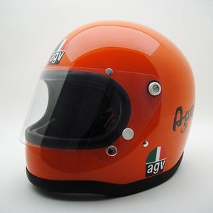 May include: Glossy orange motorcycle helmet with a clear visor and black interior. Features the "AGV" logo and script on the side. The helmet has a black trim around the base and a clear visor.