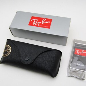 Puede incluir: Un estuche de gafas de cuero negro con un logotipo dorado, una caja gris con un logotipo rojo y un pa&ntilde;o de limpieza con un logotipo rojo. El estuche se cierra con un broche. La caja y el pa&ntilde;o tienen el logotipo de Ray-Ban.