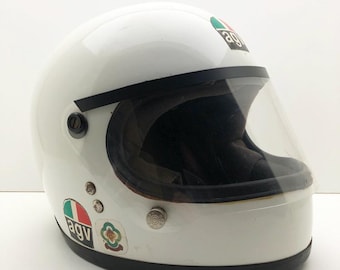 May include: White vintage motorcycle helmet with a clear visor and black trim. The helmet has several colorful stickers, including the brand logo. A classic design for motorcycle enthusiasts.