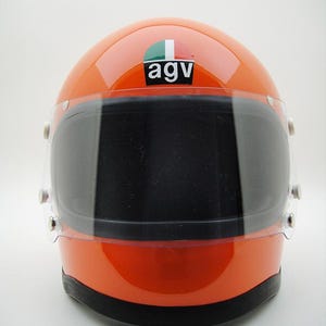 May include: Orange motorcycle helmet with a dark visor. The helmet has the logo "agv" on the top. The visor is clear and has a black tint. The helmet is a glossy orange color.