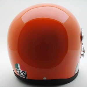 May include: Glossy orange motorcycle helmet with a black trim. The helmet features a reflective surface and a small sticker with the letters "agv" and the colors green, white, and red. The helmet is designed for safety and protection.