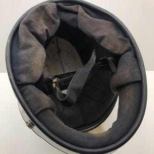 May include: A motorcycle helmet, viewed from the inside, with a black interior and chin strap. The interior padding is dark grey. The exterior is white with a black trim.