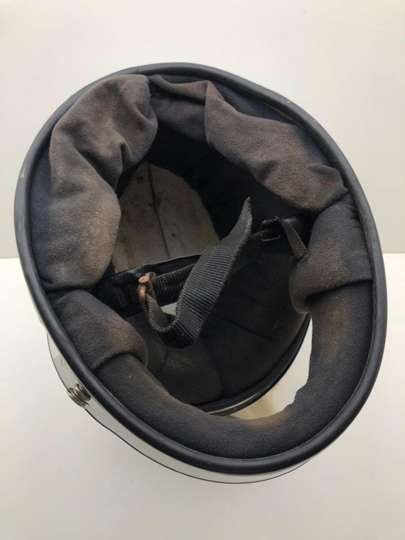 May include: A motorcycle helmet, viewed from the inside, with a black interior and chin strap. The interior padding is dark grey. The exterior is white with a black trim.