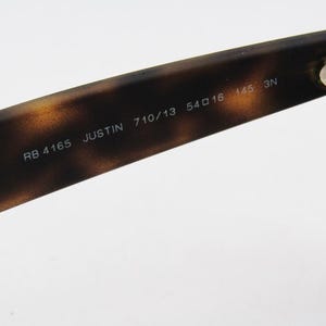 Puede incluir: Primer plano de la patilla de unas gafas de sol con un patr&oacute;n de carey marr&oacute;n. El texto "RB 4165 JUSTIN 710/13 54口16 145 3N" est&aacute; impreso en la patilla. La bisagra es visible en el lado derecho.