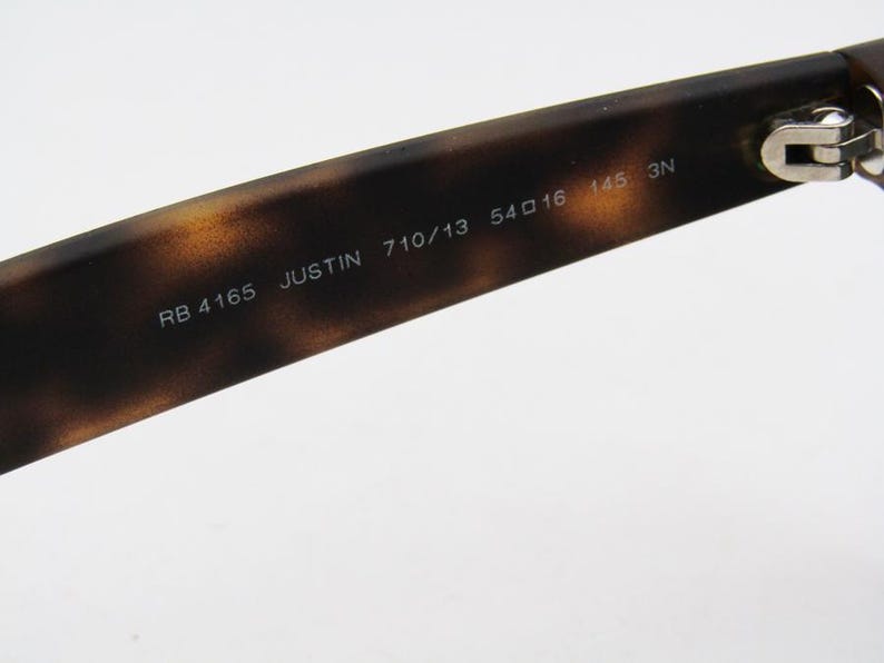 Puede incluir: Primer plano de la patilla de unas gafas de sol con un patr&oacute;n de carey marr&oacute;n. El texto "RB 4165 JUSTIN 710/13 54口16 145 3N" est&aacute; impreso en la patilla. La bisagra es visible en el lado derecho.