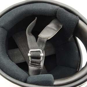 May include: Interior view of a motorcycle helmet. The helmet features a black padded interior with a chin strap and a metal buckle. The outer shell is white with a black trim.